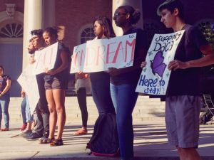 Students stand outside a building holding signs in support of DACA.