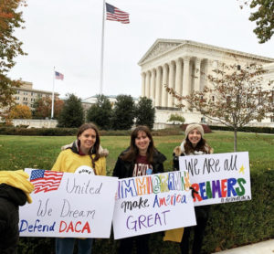 Three students stand in front of a government building. They are holding pro-DACA signs 